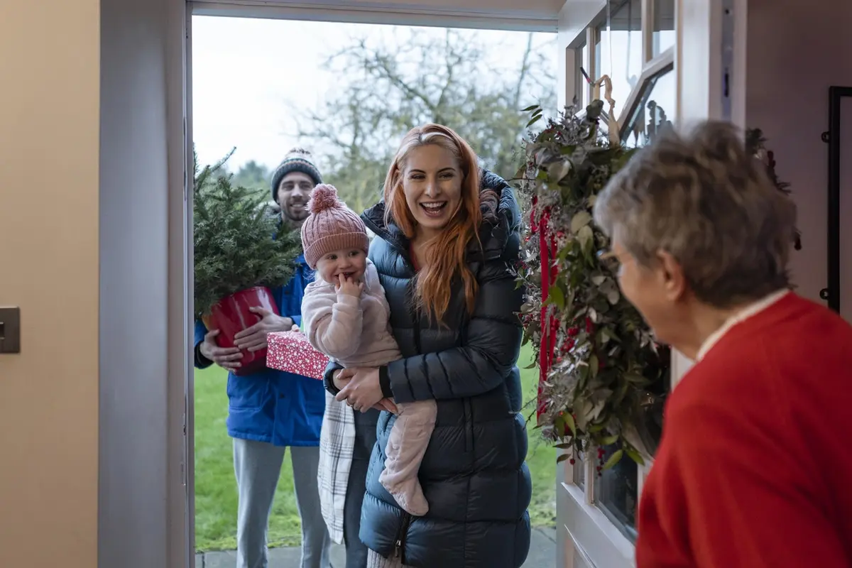 Smiling senior woman greeting a visitor with a warm hug, illustrating what is the biggest cause of loneliness and the importance of meaningful connection in later life.