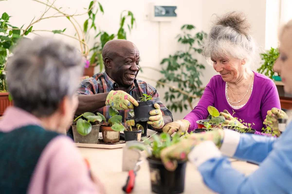 Two seniors smiling while caring for potted plants in an assisted living activities.